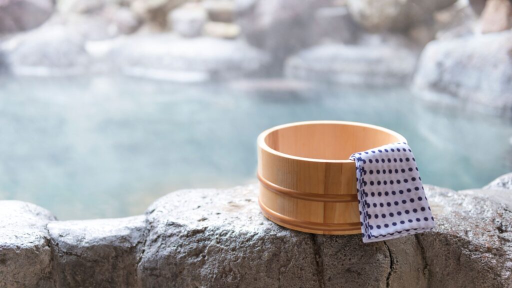 Baquet en bois de cèdre avec tissu tenugui devant un onsen