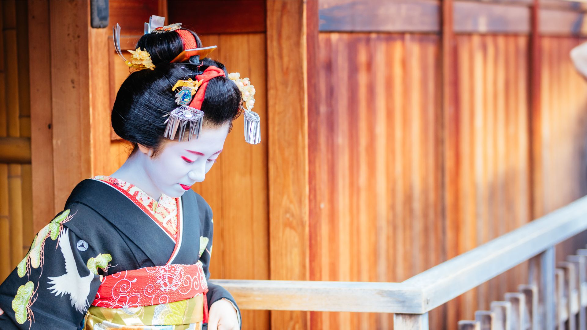 Une geisha portant des épingles à cheveux traditionnelles et une ceinture rouge émerge d'une porte en bois au Japon.